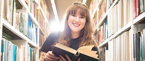 Creative writing student reading a book in library